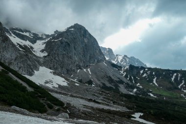 Avusturya 'daki Alp tepelerinde Marstein' dan panoramik bir manzara. Yamaçlar çoğunlukla karla kaplı. Taşlı ve keskin dağlar. Bulutlu. Çıplak yamaçlar, aşağıdaki yeşil vadi. Dinginlik ve sakinlik