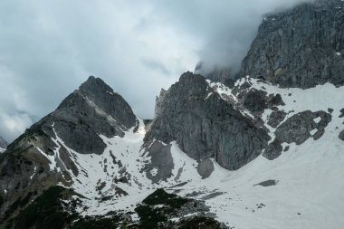 Avusturya 'daki Alp tepelerinde Marstein' dan panoramik bir manzara. Yamaçlar çoğunlukla karla kaplı. Taşlı ve keskin dağlar. Bulutlu. Çıplak yamaçlar, aşağıdaki yeşil vadi. Dinginlik ve sakinlik