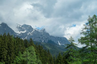 Avusturya 'daki Alp tepelerinde Marstein' dan panoramik bir manzara. Yamaçlar hâlâ kısmen karla kaplı. Taşlı ve keskin dağlar. Bulutlu. Çıplak yamaçlar, dağ eteğinde sık orman..