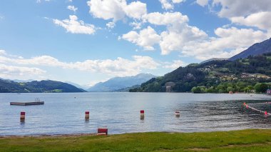Millstaettersee Gölü kıyısından panoramik bir manzara. Göl yüksek dağlarla çevrilidir. Alp gölü hafifçe el sallıyor. Yüzeyinde sürüklenen birkaç şamandıra var. Dinginlik ve sakinlik