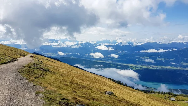 一条通往奥地利阿尔卑斯山阿尔卑斯山牧场的凹凸不平的道路 山谷笼罩在雾中 山坡上绿油油的 许多山在云彩之上翻腾 没有车辆 道路空旷 — 图库照片