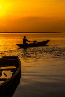 Geleneksel bir Peru teknesi, Peke Peke adlı bir kano, Amazon ormanlarında kullanılır. Gün batımında Amazon nehri manzarası. Adam Amazon Nehri 'nde tipik bir tekne kullanıyor.