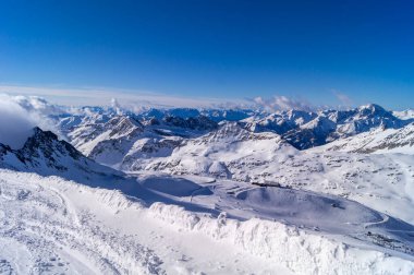 Dağlarda kar, uzakta sis, mavi gökyüzü, kayak pisti, karlı dağların manzarası.