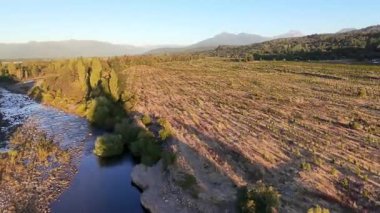Gün batımında dağlık bir arazideki bir nehrin insansız hava aracı görüntüleri.