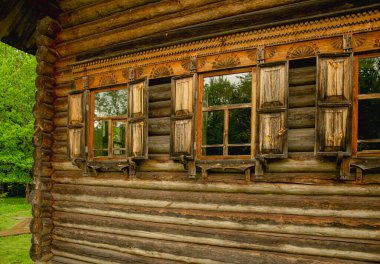 Kulübenin duvarı oyulmuş süslemelerle süslenmiş, pencereler ağaçları ve gökyüzünü yansıtıyor..