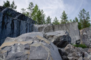 Mermer bloklar. Çam ormanıyla kaplanmış mermer bir kaya. Mavi gökyüzündeki bulutlar.