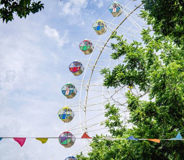 Dönme dolabın çok renkli kabinleri önlerinde büyüyen bir ağaçla gökyüzünde yükselir..