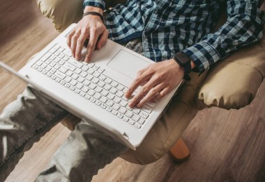 Evde dizüstü bilgisayar kullanan yakışıklı bir genç. Öğrenciler odasında dinleniyor. Çevrimiçi alışveriş, ev işi, serbest çalışma, çevrimiçi öğrenme, öğrenim kavramı. Uzaklık eğitimi