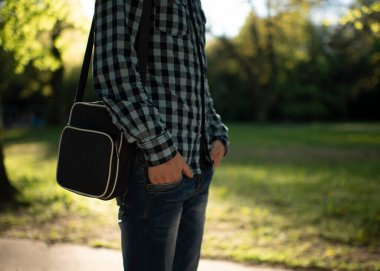 Elinde çanta olan adam yazın parkta yürür.