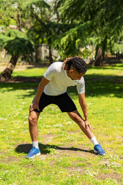 Young black man doing sports outdoors in a park, the boy is running between trees, he wears dreadlocks