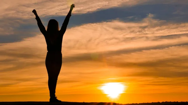 Woman silhouette with arms raised.Concept of joy and happiness, against the background of an orange sunset