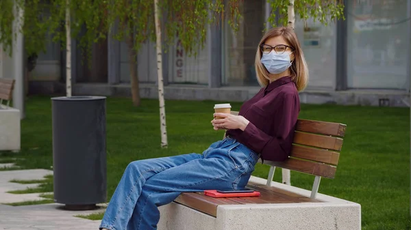Tıbbi maske takan beyaz iş kadını ara verdi. İşten dinlenme molası güneşli bahar yaz kahve molasının tadını çıkarıyor. Hanımefendi düşünceli görünüyor ve kahveden hoşlanıyor.. 