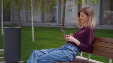 Sarışın Çekici Kadın, müzik dinlemek için kulaklık kullanırken şehirde dikiliyor. Popüler Şarkılar seçiliyor ve Müzik Uygulamaları indiriliyor. Öğle yemeği molasının tadını çıkarıyor..