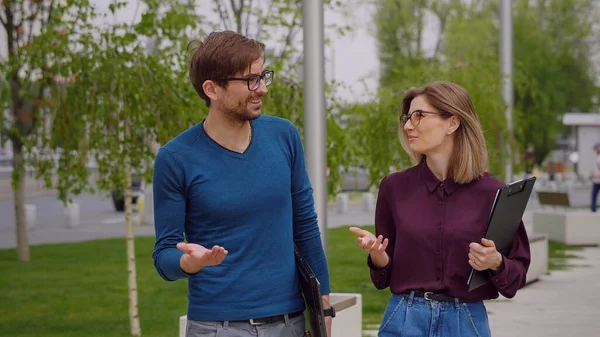 Erkek ve kadın dışarıda iş hakkında konuşuyorlar. Ortaklar arasındaki kavram. Adam dizüstü bilgisayarı elinde tutuyor, kadının elinde bir dosya var. Başarılı insanlarız. Hepsi işle ilgili. Yaz. Yavaş çekim videosu.