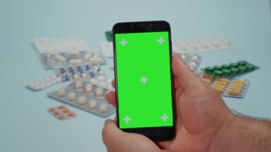 Yaklaş, akıllı telefon, yeşil ekran ve mavi arka planda tıbbi ilaçlar kullanan adam eli. İnternette akıllı telefon kullanarak bir doktorla konuşmak.