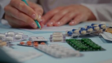 Yakın plan, masada haplar, doktor elleri reçeteyi reçeteye yazıyor. Beyaz önlüklü bir doktor