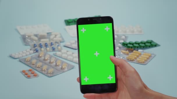 閉じるアップの女性手スワイプオンザスマートフォン緑の画面と医療用丸薬ブリスターパックオン青の背景スワイプオンザ画面 — ストック動画