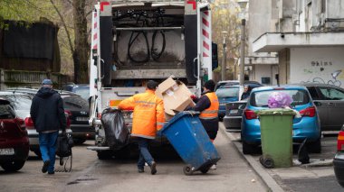 BUCHAREST, ROMANIA - 15 Mayıs 2021: Bucuresti 'de atık veya çöp toplama için kullanılan beyaz çöp kamyonu. Atık toplama kamyonuna karışık yerli atık yükleyen iki işçi