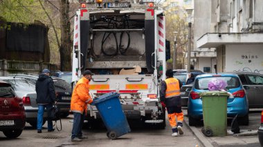 BUCHAREST, ROMANIA - 15 Mayıs 2021: Bucuresti 'de atık veya çöp toplama için kullanılan beyaz çöp kamyonu. Şehirden gelen atık kamyonuna karışık yerli atık yükleyen iki işçi