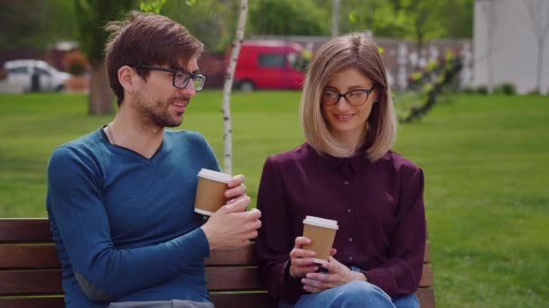 안경을 여자와 잘생긴 남자가 커피를 마시며 브레이크 작업을 즐기는 벤치에 — 비디오