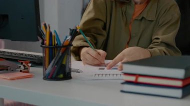 Neşeli bir kadın, dağınık ofis masasında notlar alırken telefonla konuşuyor. İş ve iletişimi dengelediği için gülümsüyor..