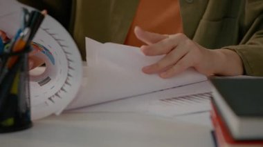Woman is focused on exploring various graph sheets in her home office. She sorts through the papers, highlighting her work during remote hours.