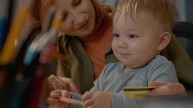 Genç anne mutlu bir şekilde internetten alışveriş yapar, çocuğunu bir kolunda dengeler ve diğer kolunda bir banka kartı. Birlikte, rahat ofislerinde dizüstü bilgisayarlarında ürünleri keşfediyorlar..