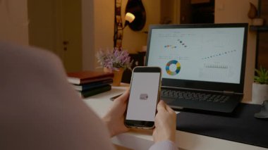 İş kadını, arka planda grafikleri gösteren dizüstü bilgisayarla akıllı telefondan online ödemeyi doğruladı