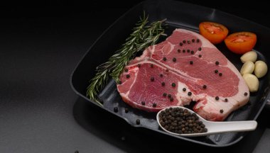 Çiğ biftek, taze otlar, sarımsak, domates, karabiber, siyah arka planda biberiye tasarımınız için fotokopi alanı, yiyecek konsepti..