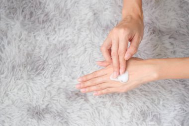 Woman applying moisturizing hand cream on hand with carpet background, Health care concept.