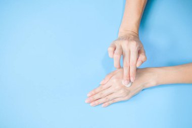 Woman applying moisturizing hand cream on hand with blue background, Health care concept.