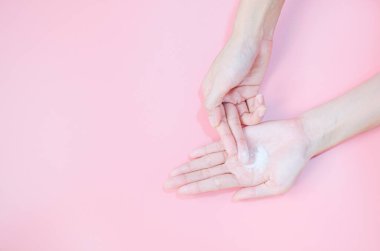 Woman applying moisturizing hand cream on hand with pink background, Health care concept.