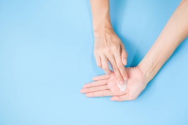 Woman applying moisturizing hand cream on hand with blue background, Health care concept.