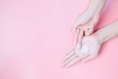 Woman applying moisturizing hand cream on hand with pink background, Health care concept.
