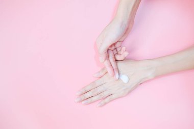 Woman applying moisturizing hand cream on hand with pink background, Health care concept.