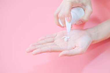 Woman applying moisturizing hand cream on hand with pink background, Health care concept.