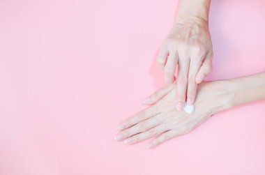 Woman applying moisturizing hand cream on hand with pink background, Health care concept.