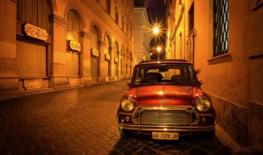 Roma, İtalya - 18 Haziran 2014. Kırmızı bir İngiliz Mini arabası gecenin geç saatlerinde geleneksel bir kaldırım taşı sokağının kenarına park edilmiş. Sokak lambaları kehribar ışığı ve derin gölgeler yaratıyor..