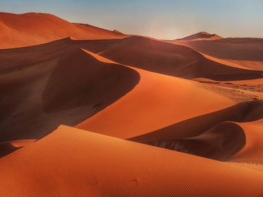 Namib Çölü, Namibya 'nın kırmızı kum tepelerinin kıvrımları, çizgileri ve gölgeleri üzerinde yükselen güneş..