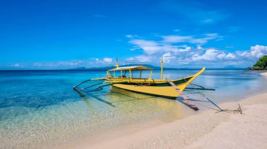 Filipinler 'de beyaz bir kumsalda, sığ bir turkuaz suya demirlemiş geleneksel Filipinli ahşap iskeleden yapılmış, tropik bir ada sahnesi..