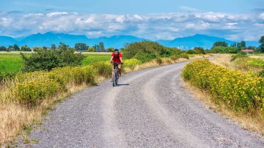 Delta, B.C., Kanada - 20 Temmuz 2019. Kasksız dağ bisikleti süren genç bir adam, güzel bir kırsal alanda çakıllı bir yolda, Vancouver şehrinin arka planında kısmen görülebiliyor..