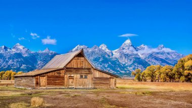Tarihi asistan manzarası. Moulton Barn, Mormon Row yolu boyunca Grand Teton Ulusal Parkı 'ndaki Antilop Düzlükleri denilen alanda, arka planda dramatik kar örtülü dağ silsilesiyle birlikte bir dönüm noktası..