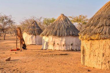 Namibya kırsalındaki Himba kabile köyünde sazdan çatıları olan üç geleneksel, yuvarlak Afrika evi..
