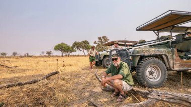 Kuzey Botswana - 29 Eylül 2014. Bir Afrika safarisi, iki safari rehberi ve bir misafir fotoğraf safarisi sırasında cip araçlarının önünde sabah molası veriyorlar..