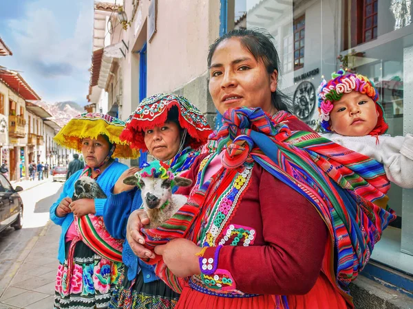 Üç Perulu kadın renkli geleneksel kıyafetler giyip ellerinde şirin kuzular ve bir bebekle Cusco 'da kaldırımda durup turistlerin fotoğraflarının çekilmesi için para ödemelerini bekliyorlar..