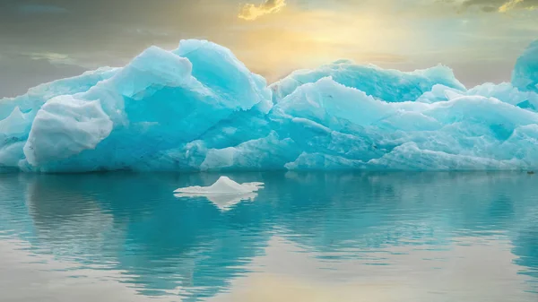 冰岛的Jokulsarlon湖中漂浮着一座美丽的绿松石冰山 天空一片漆黑 夕阳西下 衬托着温暖的色彩 — 图库照片