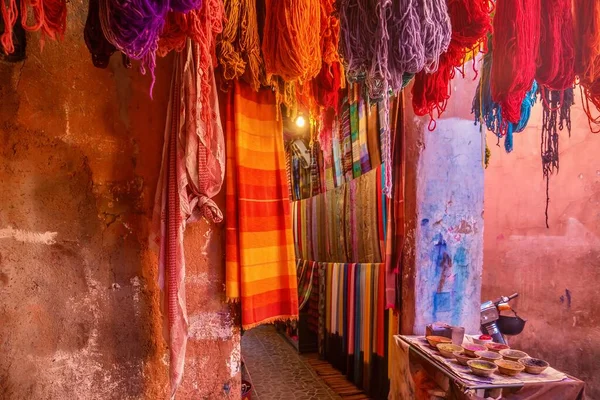 Fas 'ta bir turist dükkanının önünde renkli atkılar, iplikler ve dokulu duvarlarda boya pigmentleri olan canlı bir renk sahnesi. Marakeş 'in Medine' sinde.