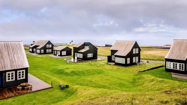 A small community of black wooden Icelandic holiday homes, which all have the same exterior design elements, on the coast of the Atlantic Ocean.