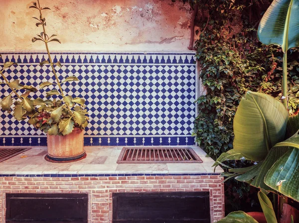 A vintage style photo of an outdoor Moroccan cooking grill in an outdoor garden setting, with a traditional blue and white tile backdrop.