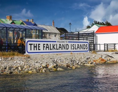 Stanley, Falkland Adaları - 25 Kasım 2010. Port Stanley 'deki hoş geldin tabelası ve yolcu gemisi yolcu indirme terminali. Arka planda renkli çatıları ve mavi gökyüzü olan antika evler var..